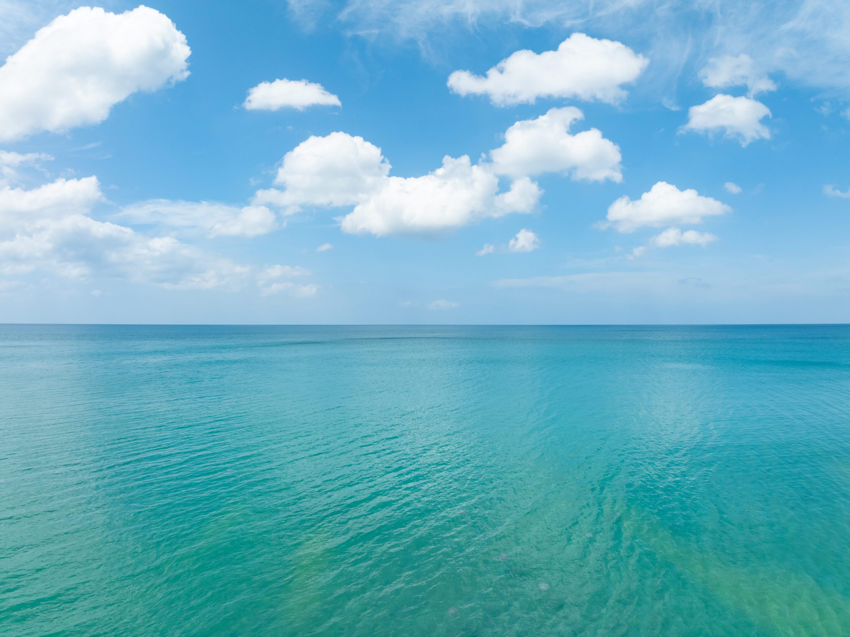 Calm ocean under a blue sky with scattered clouds.
