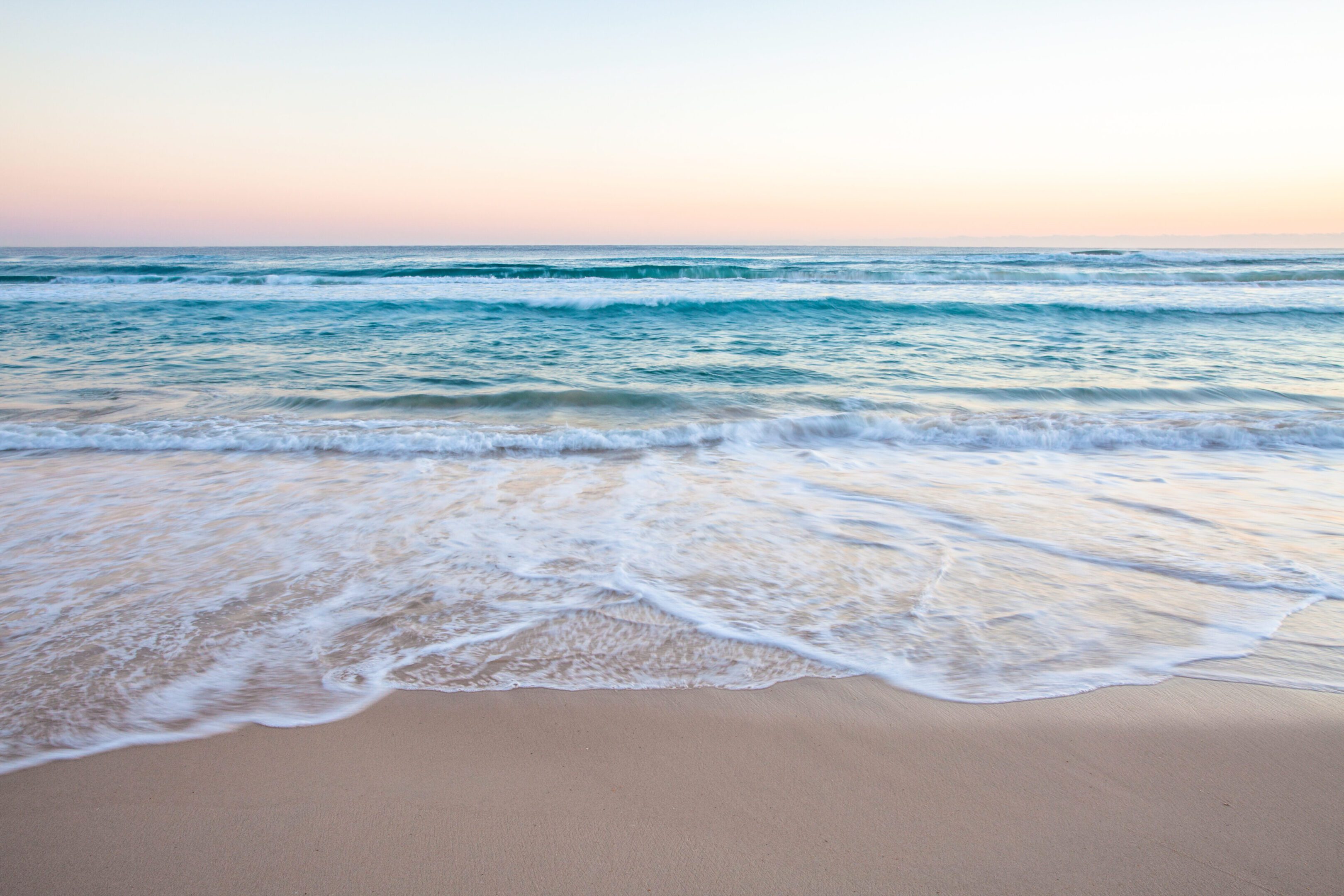 Gentle waves rolling onto a sandy beach at sunset.