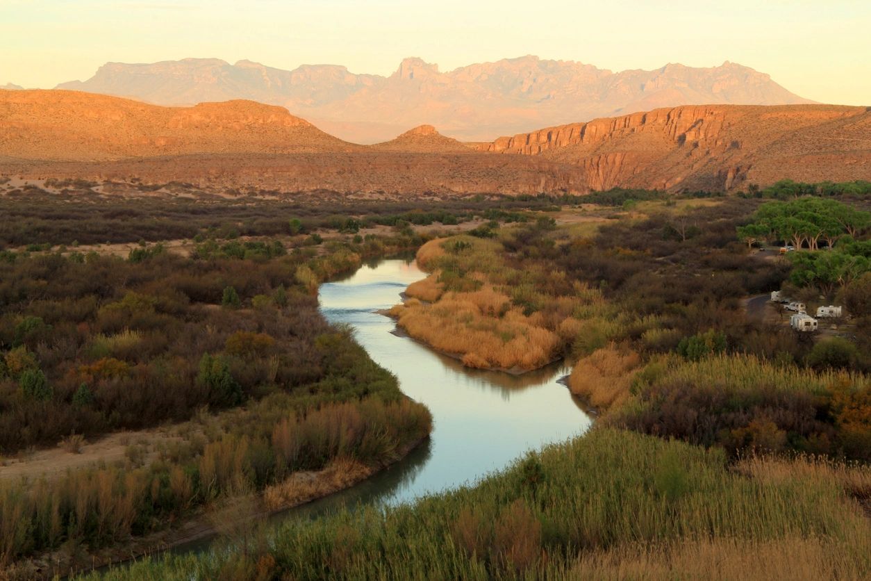 A winding river flowing through a desert landscape at sunset.
